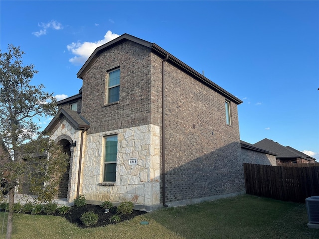 view of home's exterior with fence, a yard, brick siding, and stone siding