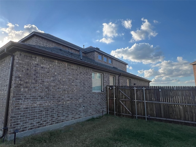 view of side of home with a lawn, brick siding, fence, and a gate