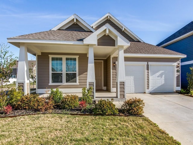 craftsman house with roof with shingles, an attached garage, a front lawn, concrete driveway, and covered porch