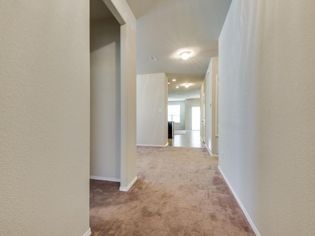 corridor featuring carpet flooring, a textured wall, and baseboards