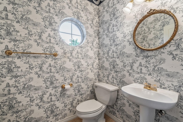 half bathroom with baseboards, wallpapered walls, and toilet