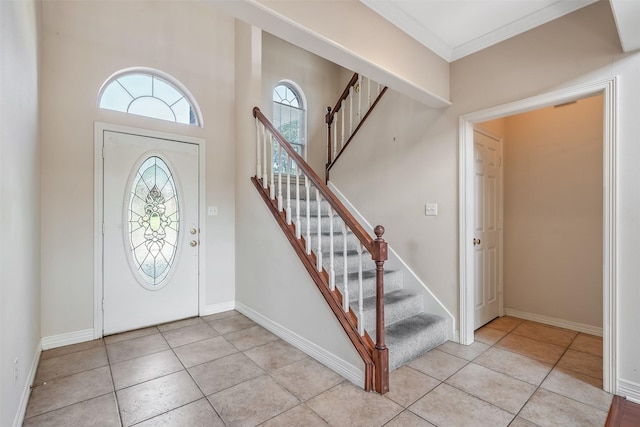 foyer featuring crown molding, baseboards, light tile patterned floors, and stairway