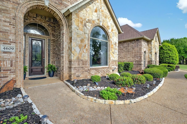 view of exterior entry with roof with shingles, stone siding, and brick siding