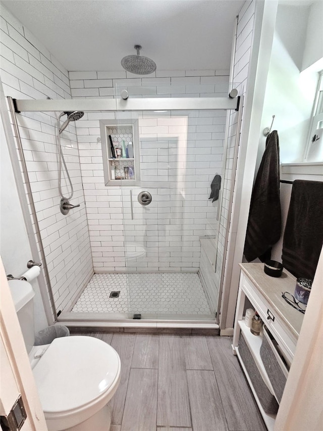 full bathroom featuring wood tiled floor, a shower stall, and toilet