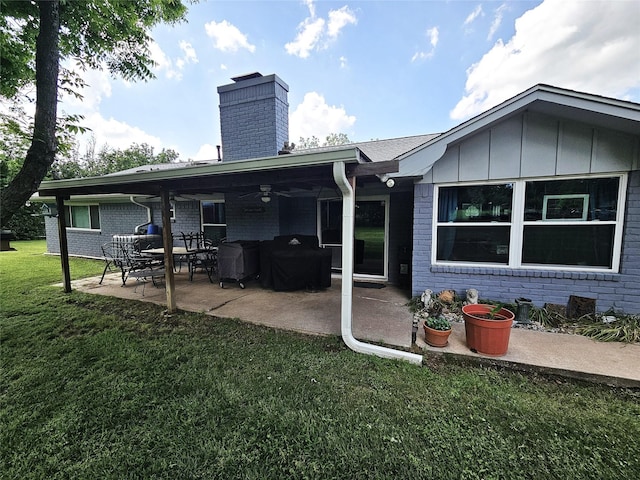 rear view of property featuring a ceiling fan, a chimney, a lawn, a patio area, and brick siding