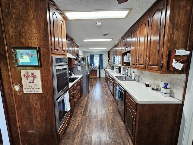 kitchen featuring dark brown cabinetry, appliances with stainless steel finishes, a sink, light countertops, and dark wood-style floors