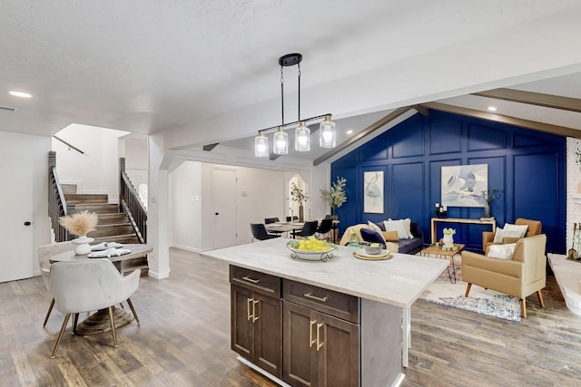 kitchen featuring pendant lighting, a decorative wall, wood finished floors, light stone countertops, and open floor plan