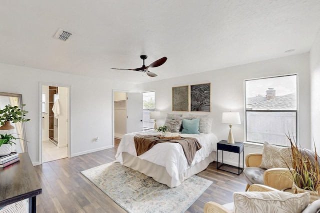 bedroom with visible vents, wood finished floors, baseboards, a spacious closet, and a ceiling fan