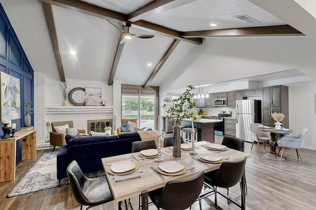 dining area featuring a fireplace, visible vents, beam ceiling, and wood finished floors