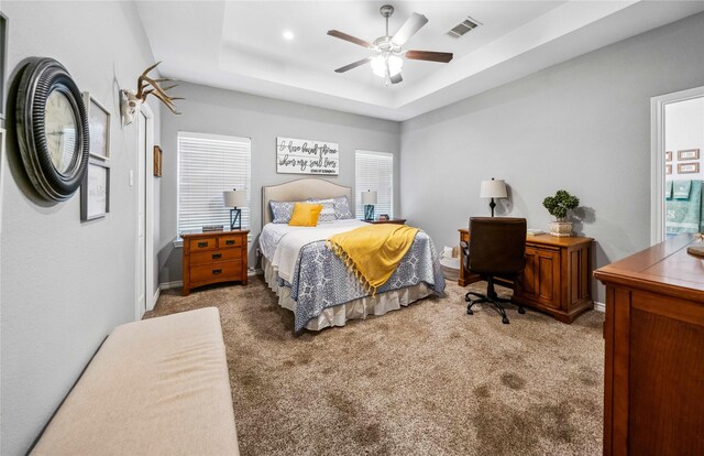 bedroom with a ceiling fan, a tray ceiling, visible vents, and carpet