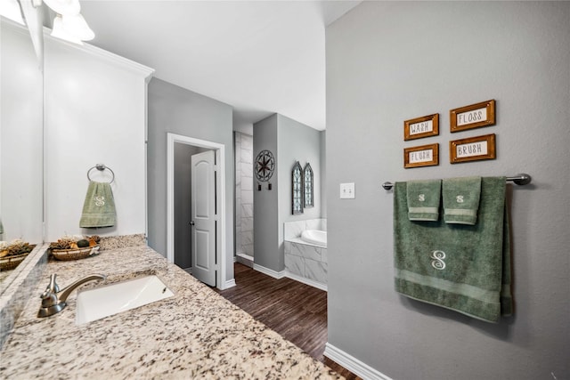bathroom with a garden tub, baseboards, wood finished floors, and vanity