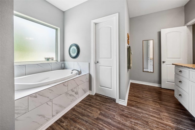 bathroom featuring a garden tub, baseboards, wood finished floors, and vanity