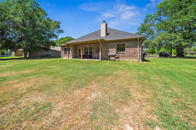 rear view of house with a shingled roof, brick siding, a chimney, a patio area, and a yard