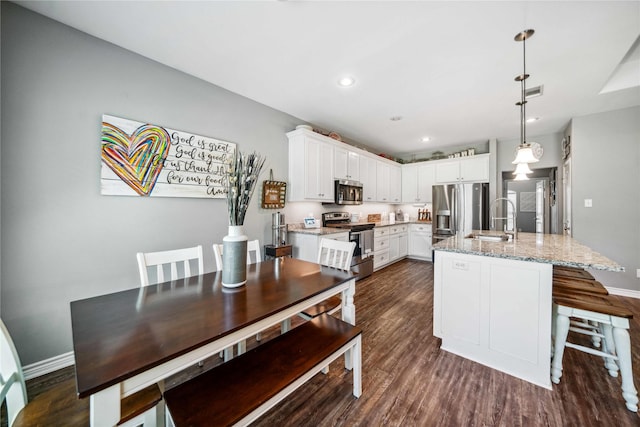 kitchen featuring white cabinets, appliances with stainless steel finishes, a sink, dark wood finished floors, and baseboards