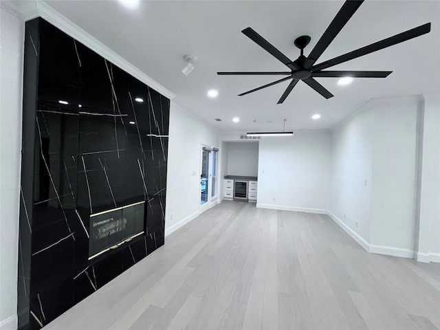unfurnished living room featuring beverage cooler, light wood-style flooring, recessed lighting, baseboards, and ornamental molding