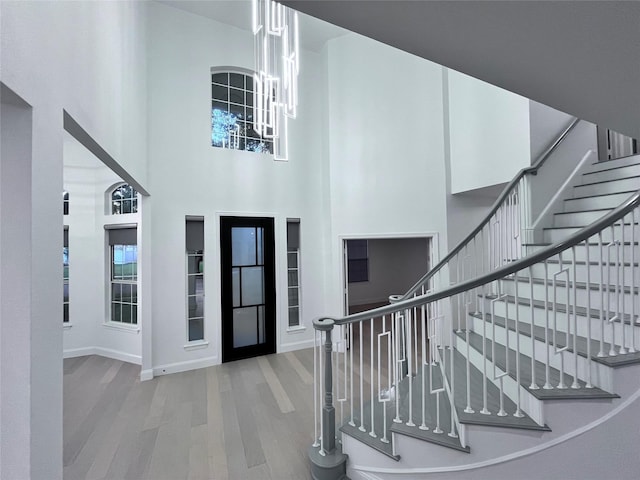 foyer featuring a chandelier, baseboards, wood finished floors, a towering ceiling, and stairway