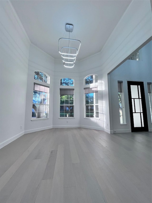 unfurnished living room featuring an inviting chandelier, baseboards, ornamental molding, and wood finished floors