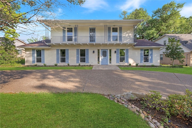view of front of house featuring a front yard, brick siding, and a balcony