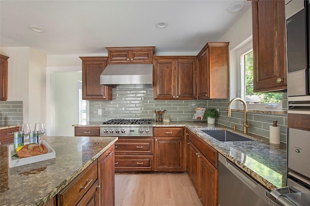 kitchen featuring a sink, dark stone counters, light wood-style floors, and stainless steel appliances