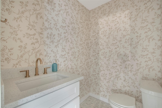 half bath featuring vanity, baseboards, toilet, and wallpapered walls