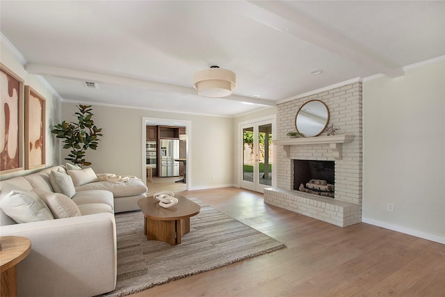 living room with crown molding, beam ceiling, a brick fireplace, wood finished floors, and visible vents