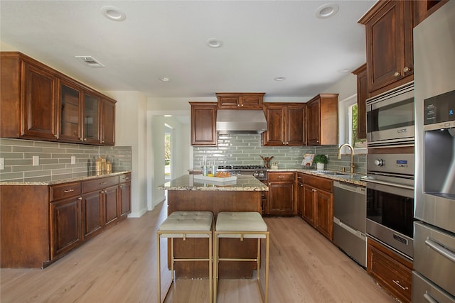 kitchen with visible vents, range hood, light wood-type flooring, appliances with stainless steel finishes, and backsplash