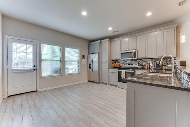kitchen featuring recessed lighting, dark stone counters, tasteful backsplash, a sink, and stainless steel appliances