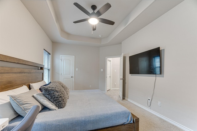 bedroom with light colored carpet, a raised ceiling, ceiling fan, and baseboards
