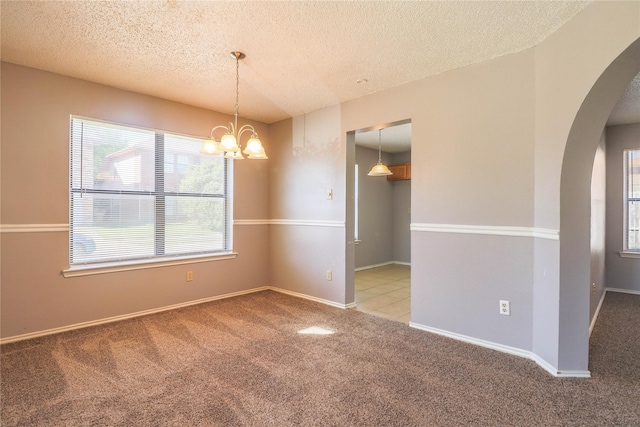 spare room featuring arched walkways, carpet, a textured ceiling, and a chandelier