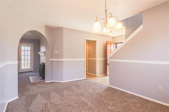 unfurnished dining area with carpet floors, arched walkways, a textured ceiling, and an inviting chandelier