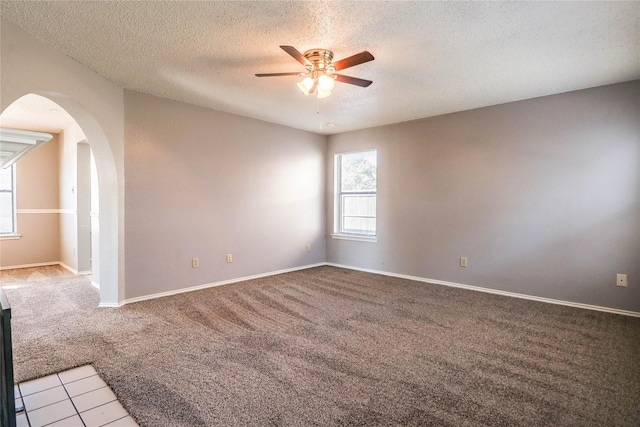 spare room featuring light colored carpet, arched walkways, a textured ceiling, a ceiling fan, and baseboards