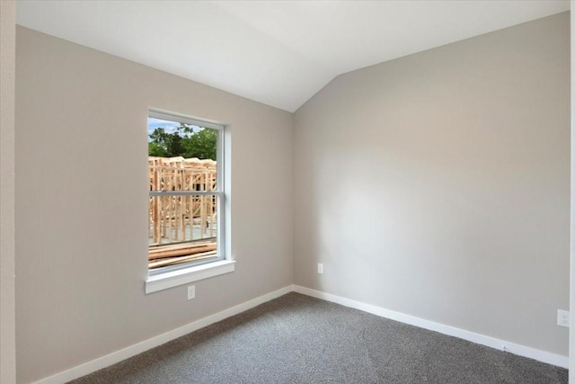 spare room with dark colored carpet, baseboards, and lofted ceiling