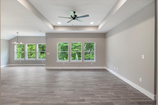 unfurnished living room featuring wood finished floors, baseboards, ceiling fan with notable chandelier, a tray ceiling, and recessed lighting