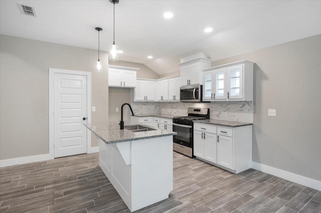 kitchen featuring wood finished floors, white cabinetry, tasteful backsplash, a sink, and appliances with stainless steel finishes