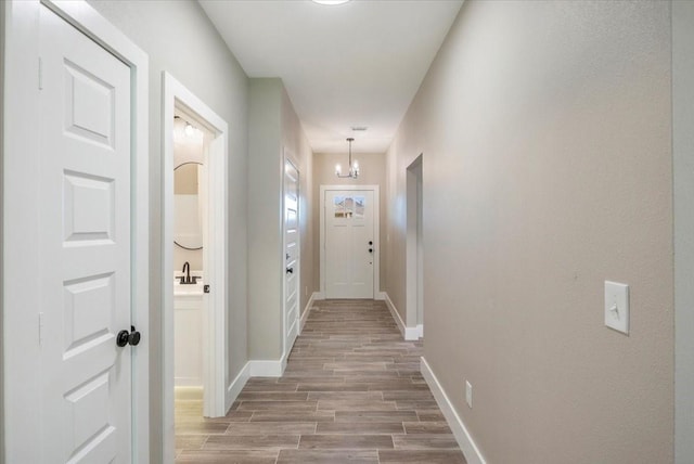 hall with baseboards, a sink, light wood-style flooring, and an inviting chandelier