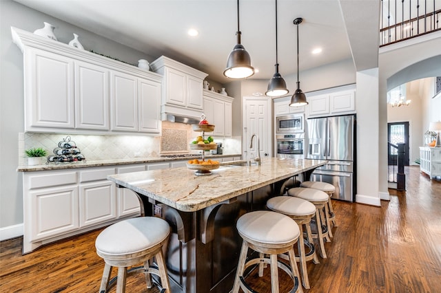 kitchen with backsplash, appliances with stainless steel finishes, arched walkways, a sink, and white cabinetry