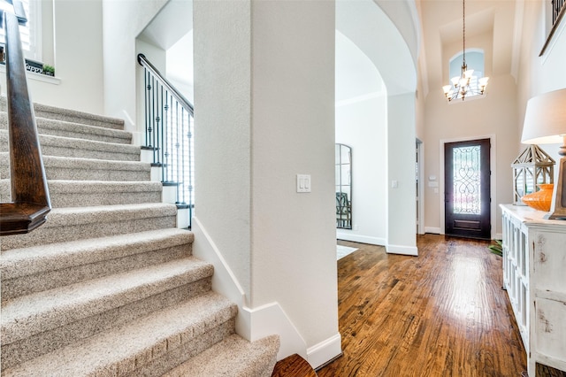 foyer with arched walkways, a chandelier, dark wood finished floors, baseboards, and stairway