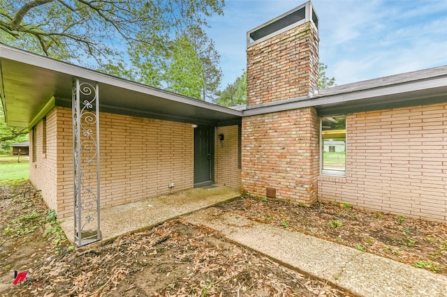 view of exterior entry featuring a chimney and brick siding