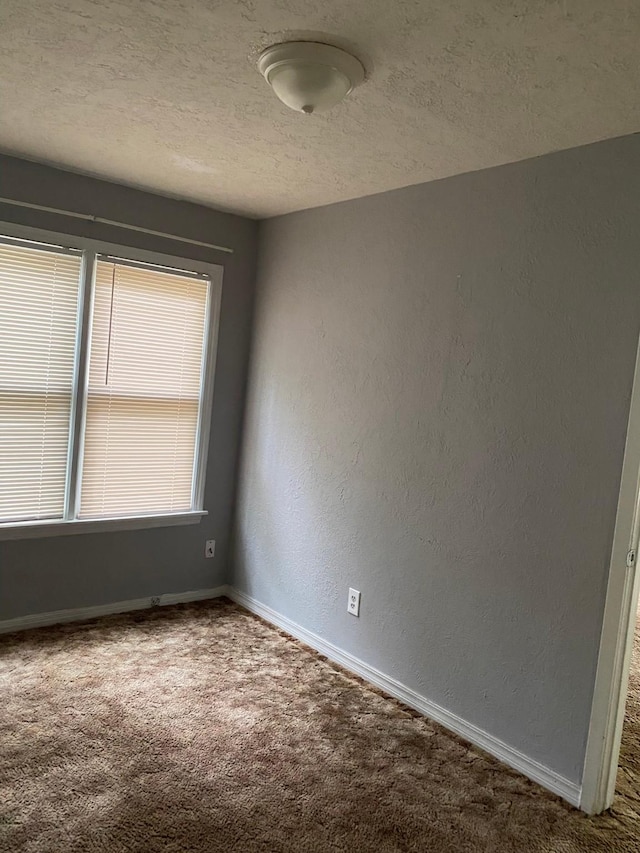empty room featuring carpet floors, a textured wall, baseboards, and a textured ceiling