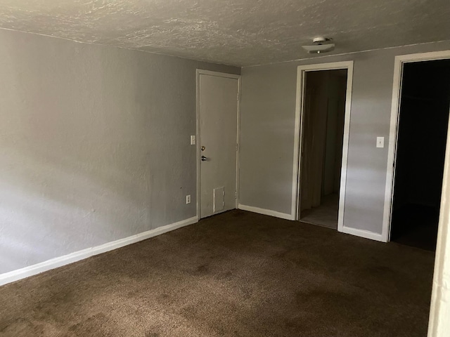 spare room with a textured ceiling, baseboards, and dark colored carpet