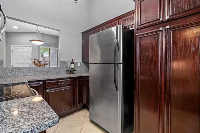 kitchen with freestanding refrigerator, dark brown cabinets, light tile patterned flooring, and hanging light fixtures