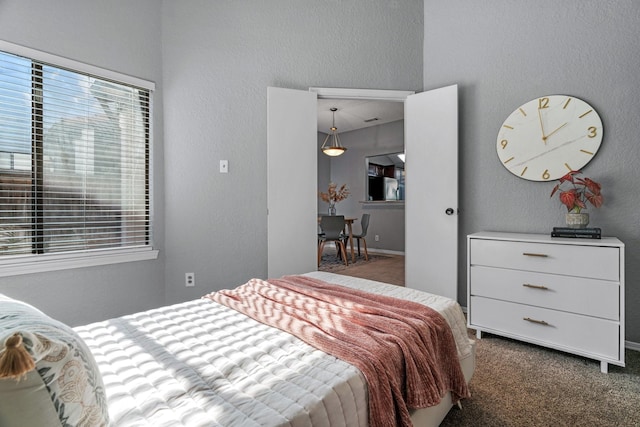 carpeted bedroom with freestanding refrigerator and a textured wall