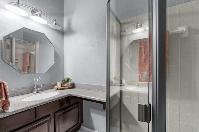 full bath featuring vanity, a textured wall, and a stall shower
