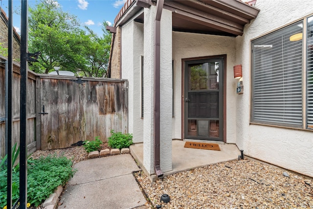 view of exterior entry with fence and stucco siding