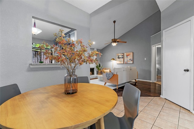 tiled dining room featuring a ceiling fan, lofted ceiling, and a warm lit fireplace