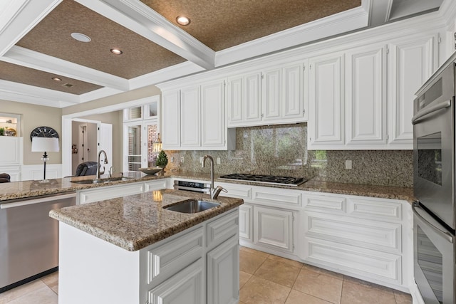 kitchen featuring appliances with stainless steel finishes, a sink, stone countertops, decorative backsplash, and ornamental molding