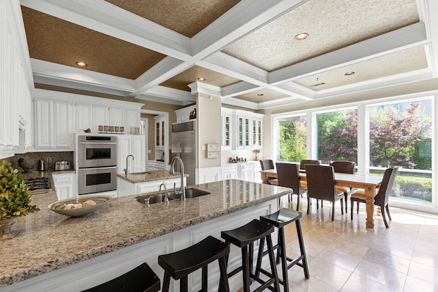 kitchen with a sink, coffered ceiling, stainless steel appliances, and a peninsula