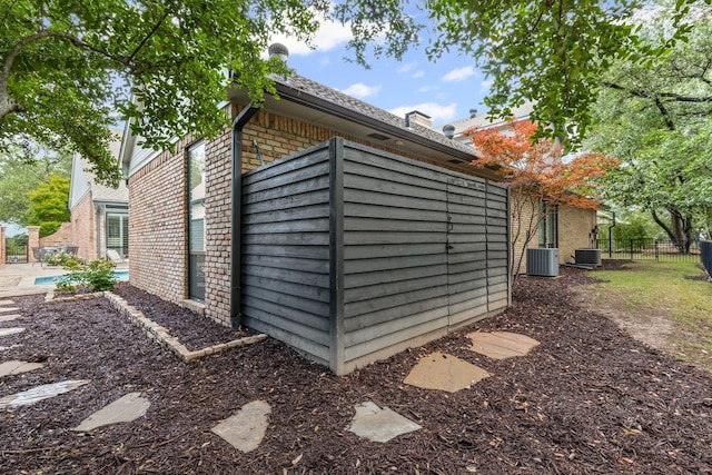 view of outdoor structure with fence, central AC unit, and an outdoor pool