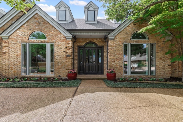 doorway to property with a shingled roof and brick siding