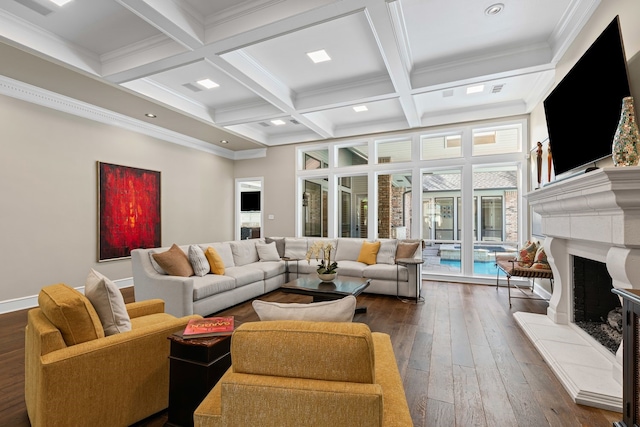 living area featuring dark wood finished floors, beamed ceiling, a fireplace with raised hearth, ornamental molding, and coffered ceiling